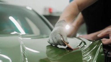 Plastik kartlarla arabanın kaputunu koyu yeşil renge sarma işlemi. Bir araba stüdyosunda araba kaputu sarma işlemi. Parlak haki rengi yeşil araba plastiği. Yüksek kalite 4k görüntü