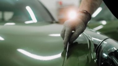 Plastik kartlarla arabanın kaputunu koyu yeşil renge sarma işlemi. Bir araba stüdyosunda araba kaputu sarma işlemi. Parlak haki rengi yeşil araba plastiği. Yüksek kalite 4k görüntü