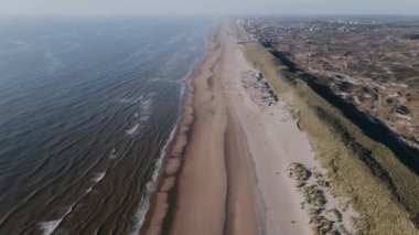 İnsansız hava aracı güneşli bir günde şehrin dışındaki okyanus kıyısında uçar. Sakin, açık mavi okyanus ve küçük dalgalar. Güneşli bir günde plaj evleri olan beyaz okyanus manzarası. Yüksek kalite 4k görüntü
