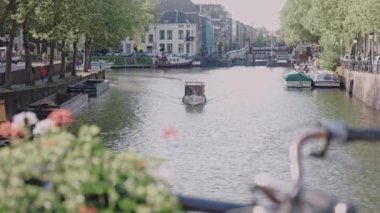 Güneşli bir günde eski tuğlalı evlerle kanala açılan küçük bir tekne. Amsterdam Kanalı 'nda sakin bir sabah. Hollanda 'daki kanalın üzerinde yeşil ağaçlar asılı. Yüksek kalite 4k görüntü