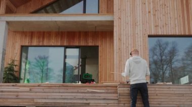 Modern bir çiftlik evinin dışında ahşap bir proje üzerinde çalışan bir adam. Ahşap bir evin şantiyesinde tahta testereyle odun kesen adam. İskandinav Barnhouse 'unun inşaatı. Yüksek kalite 4k görüntü