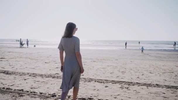 在多风的晴天 一个女人在海滩上散步 海滩上凉爽而阳光明媚的一天 在海滩上拍的女人的面色 高质量的4K镜头 — 图库视频影像
