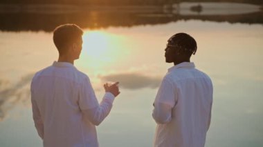 Yakışıklı genç erkekler gün batımını sahilde geçirir, vapur ve içki içerek. Arkadaşları göl plajı partisinde sohbet ediyor. Zenci adam plaj partisinde bir arkadaşıyla konuşuyor. Yüksek kalite 4k görüntü