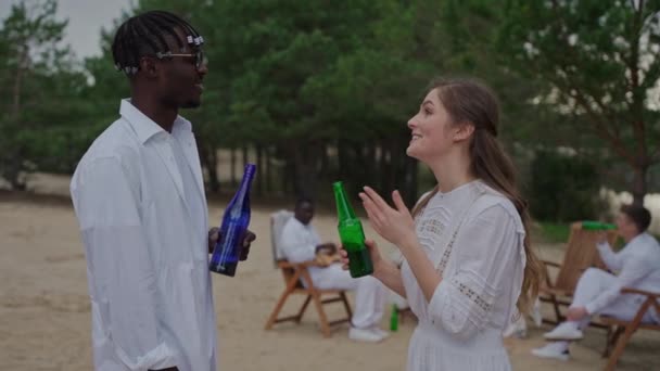 一对情侣在营地里谈情说爱 人们在日落时在森林里举行聚会 穿着白衣的人喝酒 玩得很开心 高质量的4K镜头 — 图库视频影像