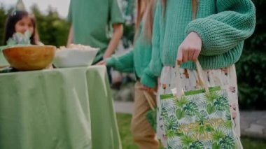 Arka bahçede bir doğum günü partisinde elinde yeşil bir hediye çantası tutan küçük bir kız. Yeşil temalı çocuklar dışarıda parti veriyor. Hediyeyle çanta sallayan, giyen bir kız. Yüksek kalite 4k görüntü