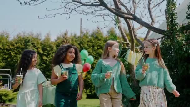 在一个阳光灿烂的日子里 有四个女孩在后院聚会上喝酒 绿色主题的生日派对 生日宴会上 孩子们笑着对着镜头说话 高质量的4K镜头 — 图库视频影像