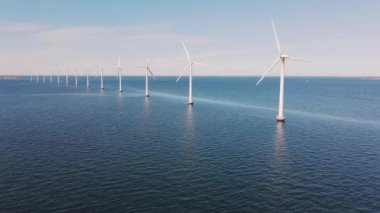 Drone flies towards an offshore windmill row in the ocean. Windmills factory in Sweden. Green energy and protection of the environment. Blue ocean and sky. High quality 4k footage