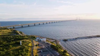 Aerial view of Oresund bridge at the sunset in summer. Cinematic shot a shore and bridge between Sweden and Denmark. Oresund bridge with a parking at the shore. High quality 4k footage