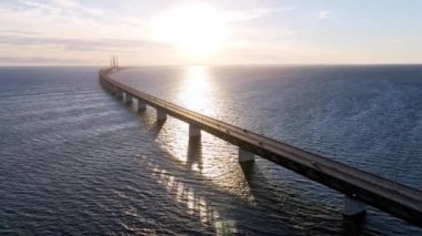 Aerial view of Oresund bridge at the sunset in summer. Cinematic shot of long bridge between Sweden and Denmark. Sunset over the sea and huge bridge. High quality 4k footage