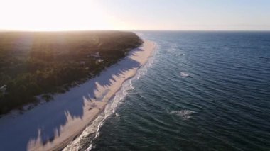 Drone flies over island with wild forest in ocean. Active sea waves come to the shore of a tropical peninsula. Dynamic aerial shot of sand beach with blue waves. High quality 4k footage