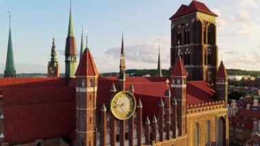 Camera flying over a gothic medieval castle with high spires and a clock in warm sunset light. Aerial shot of red brick cathedral in the center of european city. High quality 4k footage