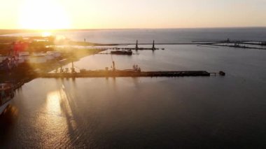 Aerial view of an industrial port with cargo ships with containers at sunset. Sun setting at the sea. Camera flying over port with shipping containers. High quality 4k footage