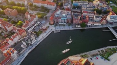 The camera flies over the center of a European city with canals and trees. Yacht sailing in canal with trees and houses. Aerial shot of red roof houses in the sunset light. High quality 4k footage