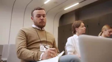 Erkek işçi bir konferanstan notlar yazıyor, sandalyeye oturuyor. Meslektaşlar eğitim seminerinin tadını çıkarıyor. Bir iş konferansından not alıyorum. Yüksek kalite 4k görüntü