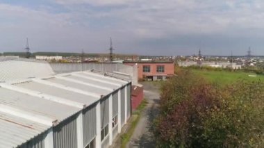 Sanayi bölgesindeki bir metal profilinden bir katlı atölyenin insansız hava aracı görüntüsü. Ağaçların ve diğer atölyelerin yanında. Helikopter bina boyunca uçuyor. Yaz güneşli bir gün