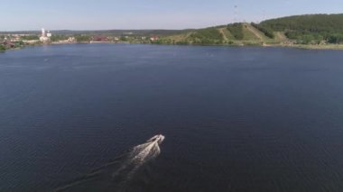 Taşra şehrindeki gölette uçan bir adamın görüntüsü. İnsanlar sörf ve raket sörfünde (SUP). Kilise, Eski Fabrika, orman, dağ ve sahildeki şehir plajı. Yaz güneşli bir gün