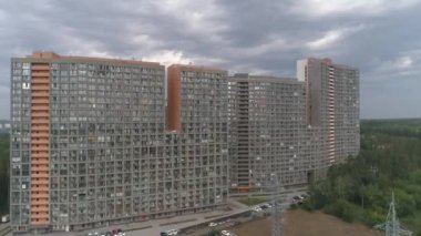 Bulutlu bir günde apartmanların insansız hava aracı görüntüleri. Ormanla çevrili park yeri ve arabalarla birlikte kamu binasının üzerinde havadan çekilmiş bir fotoğraf. Yeni bir apartmanın dış cephesi. Geniş pencereli, balkonlu yüksek binaların modern tasarımı.