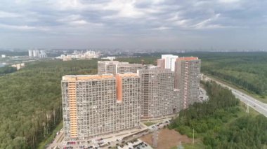 Bulutlu bir günde otobanın yanındaki binaların insansız hava aracı görüntüleri. Ormanla çevrili park yeri ve arabalarla birlikte kamu binasının üzerinde havadan çekilmiş bir fotoğraf. Kasvetli bulutlu gökyüzü. Otoyolda sürüş yapan bir sürü araba var.