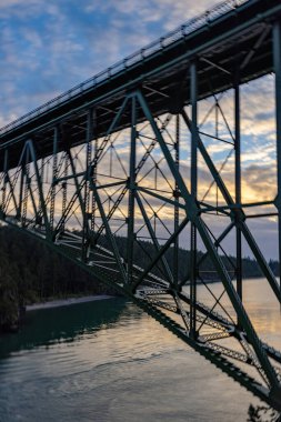 Okyanus üzerinde bulutlu bir gün batımı bir köprünün iskeletinde