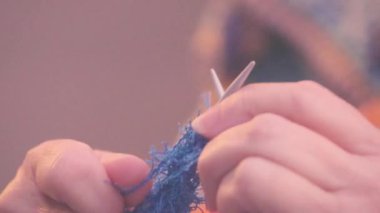 Yaşlı kadın elleri mavi iplikle örgü örüyor