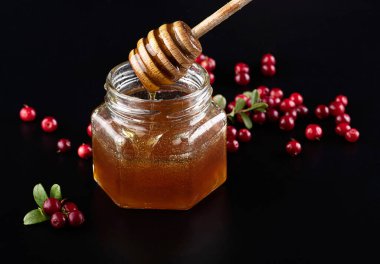 Güzel şeffaf bal kaşıktan cam kavanoza akıyor. Masaya serpilmiş taze taze kızılcık ve yabanmersini dalı. Yansıması olan siyah bir arkaplanda