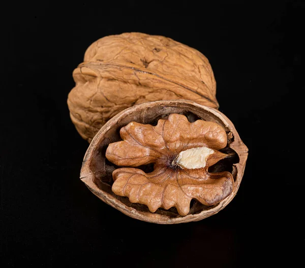 Kabuklu güzel bir ceviz ve siyah bir arka planda yarım ceviz ve yansıması var.