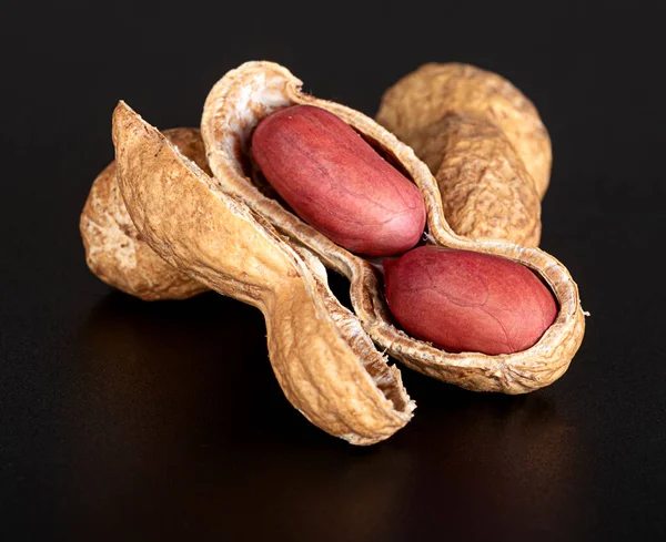 Güzel, taze, parçalanmış kabuklu fıstıklar içinde parlak, güzel fındıklar ve parlak siyah bir arka planda yansıması olan bir sürü fındık. Yakın plan. Üst görünüm