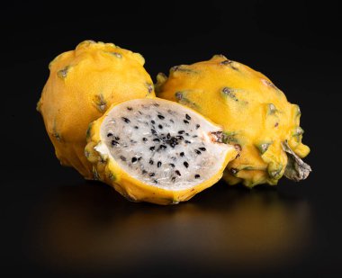 Tam ve doğranmış sarı, ballı ejderha meyvesi parlak siyah bir arka planda yansımalı.