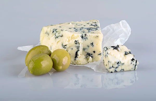 青いカビ ゴルゴンゾーラ ロックフォール スティルトン ダンブルン とおいしい香りのチーズの作品反射と光沢のある白い背景に白いクラフト紙に大きな緑のオリーブ — ストック写真
