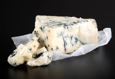 Mavi küflü lezzetli bir peynir parçası (Gorgonzola, Roquefort, Stilton, Danablouin) parlak siyah arka planda beyaz bir kağıt üzerinde yansıması olan