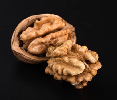 Bir kabuktaki ceviz çekirdekleri ve siyah bir arka planda kabuk olmadan.