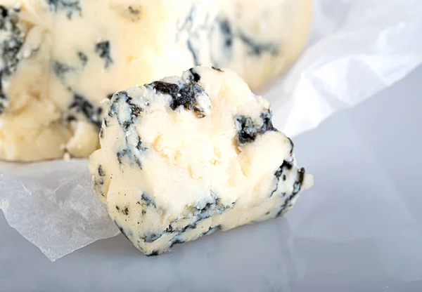 白いクラフト紙にブルーの型を持つチーズの大きな部分からカットされた青い型のチーズは 白い背景に隔離されています — ストック写真