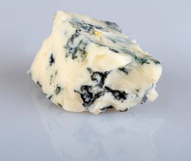 Beyaz bir arkaplanda yansıması olan mavi küflü bir peynir parçası.