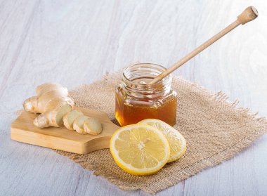 Bal için bir kaşıkla cam kavanozda bal. Taze doğranmış zencefil ve çuval bezinde limon dilimleri.