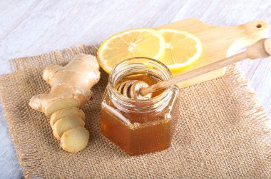 Bal için bir kaşıkla cam kavanozda bal. Taze doğranmış zencefil ve çuval bezinde limon dilimleri.