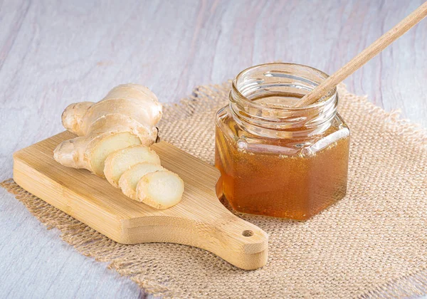 Bal için bir kaşıkla cam kavanozda bal. Çuval bezinde taze doğranmış zencefil