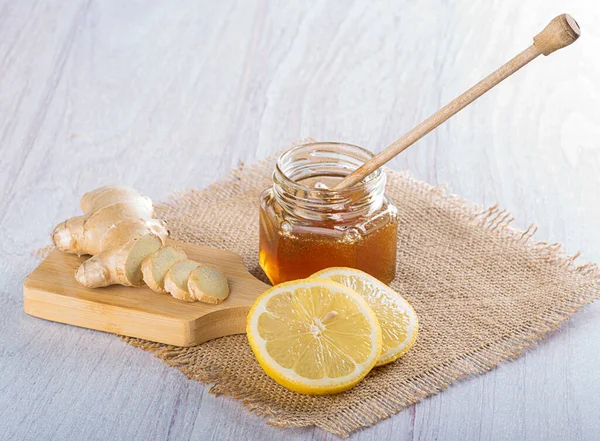 Bal için bir kaşıkla cam kavanozda bal. Taze doğranmış zencefil ve çuval bezinde limon dilimleri.