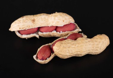 Kabuklu ve kabuksuz bütün yer fıstıkları, yansıması olan siyah bir arkaplanda izole edilmiş.