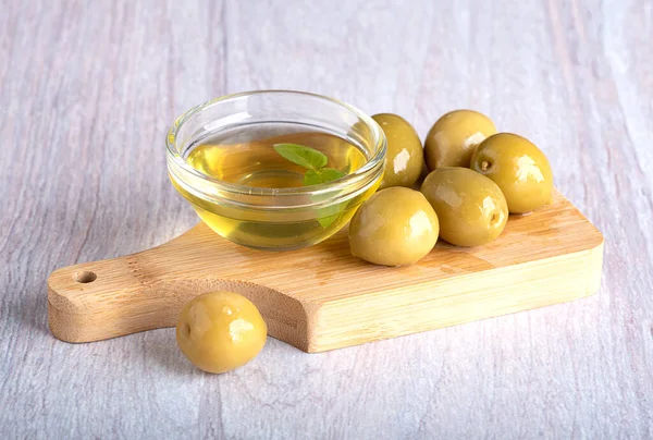 Cam kasede zeytinyağı, tahta kesme tahtasının üzerinde yeşil zeytin.