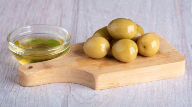 Large green olives on a wooden chopping board. Olive oil in a glass bowl