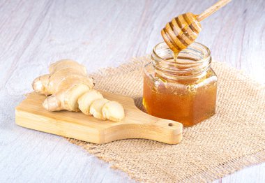 Bal için bir kaşıkla cam kavanozda bal. Hafif ahşap zemin üzerinde taze dilimlenmiş zencefil
