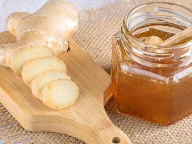 Bal için bir kaşıkla cam kavanozda bal. Hafif ahşap zemin üzerinde taze dilimlenmiş zencefil. Üst görünüm, Yakın plan