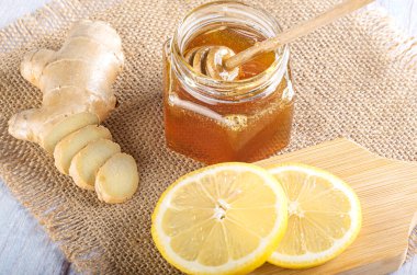 Bal için bir kaşıkla cam kavanozda bal. Çuval bezinde taze zencefil ve limon dilimi. Üst görünüm