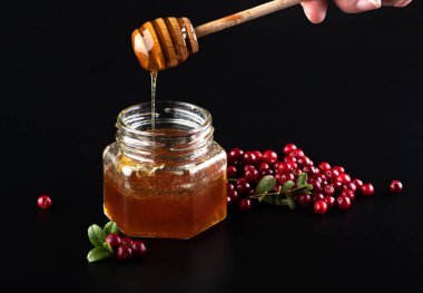 Bal kavanoza dökülüyor ve siyah arka planda yaban mersini var.