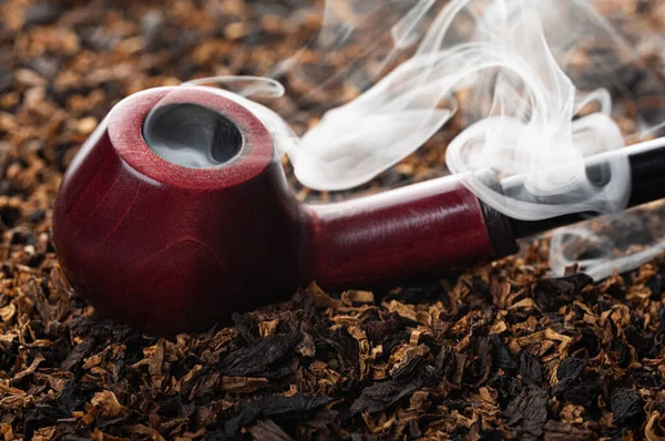 Tütünün arka planında güzel duman akıntıları olan ahşap sigara piposu. yakın plan.