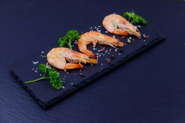 Siyah arkaplanda maydanozlu, tuzlu ve biberli büyük çiğ karidesler.