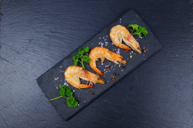 Siyah zemin üzerinde maydanozlu, tuzlu ve biberli büyük çiğ karidesler. Üst görünüm