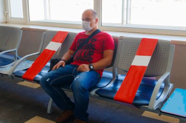 Tıbbi maske takan ve havaalanında uçuş için bekleyen bir adam. Pandemik ve kişisel koruma süresince seyahat kavramı