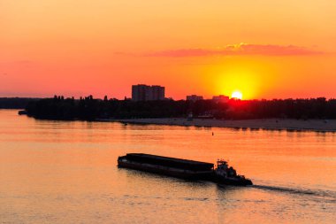 Römorkör, gün batımında Dinyeper nehrinde ağır, uzun bir mavnayı itiyor.