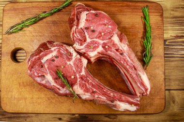 Kemiğin üzerinde çiğ biftek, baharatlar ve ahşap masada biberiye. Üst görünüm